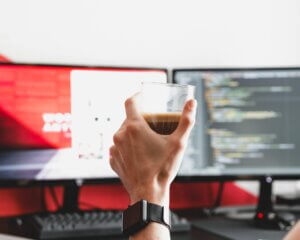Dłoń trzymająca kubek z kawą na tle monitorów