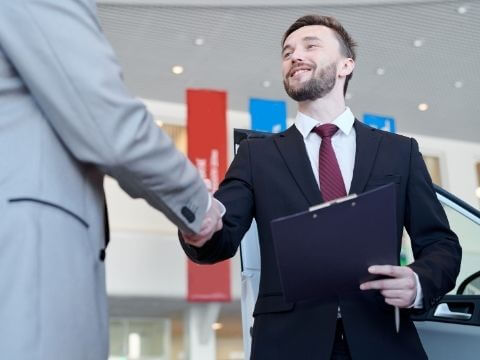 Mężczyzna w garniturze ściskający dłoń drugiej osoby.